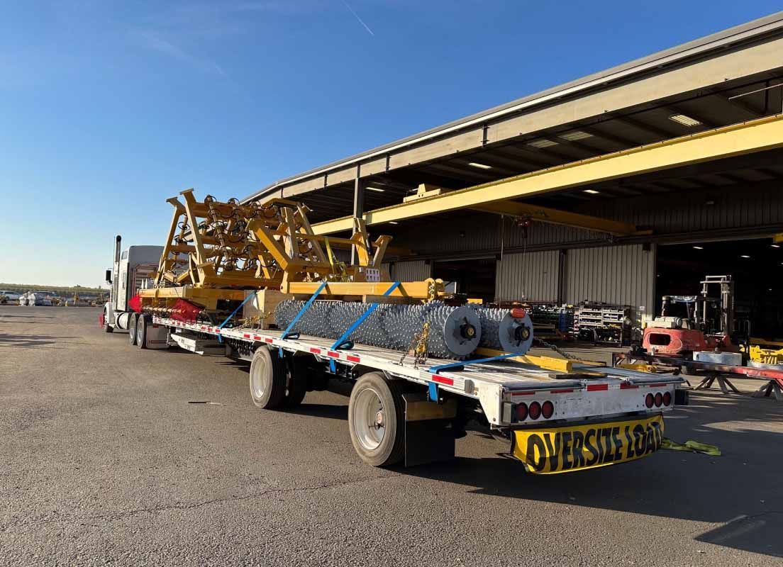 An oversized load of various equipment and materials strapped to a truck bed at a facility.