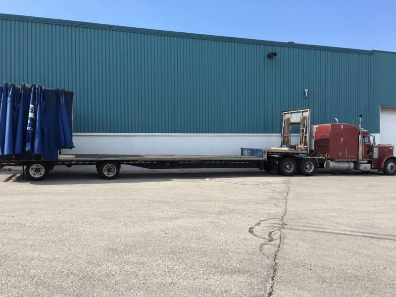 A long truck with an empty low flat bed in front of an industrial building.
